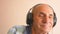 Happy Caucasian pensioner in headphones dances and listens to music. Home leisure of an elderly person dancing merrily. A man over