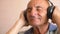 Happy Caucasian pensioner in headphones dances and listens to music. Home leisure of an elderly person dancing merrily. A man over