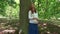 Happy caucasian pregnant girl stroking her belly standing near big tree trunk