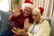 Happy caucasian senior couple in santa hats having christmas smartphone video call waving at home