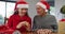 Happy caucasian senior father and adult daughter wearing santa hats making video call opening gift