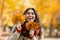 Happy Caucasian woman with bunches of yellow fall leaves laughing at park