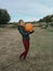 Happy Caucasian woman in jacket and red pants on farm carrying holding huge giant orange pumpkin