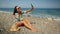 Happy caucasian woman sitting on beach by sea and taking selfies on smartphone. Carefree surf girl with waving brown hair making p