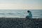 Happy caucasian woman working on a laptop while sitting on a pebble beach.