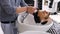 Happy charismatic young man at the barber shop while the man washes his hair.