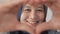 Happy cheerful Asian muslim woman smiling to camera while framing her face with heart shape made with her fingers