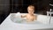 Happy cheerful baby boy happily playing and washing in the black bath. Joy and excitement of bath time for babies