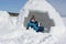 Happy cheerful boy with a piece of snow in his hands sitting an igloo