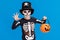 Happy cheerful boy in skeleton costume with pumpkin basket celebrates Halloween and scary gesture on blue background