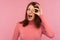 Happy cheerful brunette woman in pink sweater having fun holding crypto coin near her eye and winking looking at camera, bitcoin