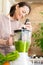 happy and cheerful caucasian woman in a t-shirt in her kitchen makes a green smoothie