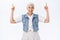 Happy, cheerful charming grandmother, senior lady smiling and laughing carefree, raising hands, pointing fingers up