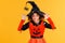 Happy cheerful ethnic girl in a pumpkin costume scary gestures and celebrates Halloween and laughs on yellow background