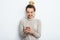 Happy cheerful glad woman with hair bun nude makeup wearing in sweater standing indoors with her smartphone chatting with friends