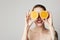 Happy cheerful tattoed young woman is holding two halves of an orange fruit in front of her eyes.