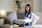 Happy cheerful young asian woman sitting on sofa with laptop, smart beautiful young asian woman chilling in house with