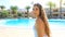 Happy cheerful young woman in white swimsuit and sunglasses on head looking at camera next to swimming pool in summer vacation in