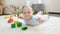 Happy cheerfull baby boy lying on floor next to colorful toys, bricks and blocks at playroom. Concept of children
