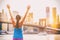 Happy cheering fit woman achieving fitness goal in New York City with arms up at sunset and Brooklyn Bridge. Girl runner