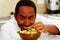 Happy chef wearing white clothes preparing bowl of food in professional kitchen, smiling while finishing last touch