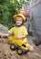 Happy child 4-5 years old in a construction helmet plays with a toy bulldozer near a pile of earth