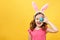 Happy child in bunny ears holds an easter blue egg. Portrait of a little girl on a yellow background