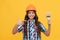 happy child with curly hair in construction helmet pointing finger on painting brush, renovation