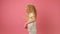 Happy child emotionally jumps on pink studio background. Slow motion portrait blonde happy caucasian teenage girl in