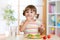 Happy child girl eats vegetables sitting at table