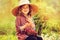 Happy child girl in hat and plaid dress picking strawberries on sunny country walk