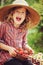 Happy child girl in hat and plaid dress picking strawberries on sunny country walk