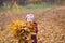 Happy child, girl holding an armful of autumn yellow leaves on the nature walk outdoors