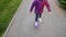 Happy child girl in jacket is rolling on purple skateboard on street in park.