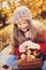 Happy child girl in knitted scarf and sweater with basket on autumn walk in forest eating apples