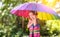 Happy child girl laughs and plays under summer rain with an umbrella.