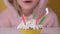 Happy child girl in pink Overalls blowing out five candles on birthday cake at party. Close up on girl face in glasses