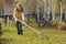 Happy child girl playing little gardener in autumn and picking leaves into basket. Seasonal garden work