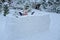 Happy child girl playing in snow castle in dropping snowballs on winter backyard