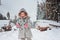 Happy child girl plays in winter snowy forest with tree felling on background