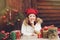 Happy child girl in red hat and scarf wrapping Christmas gifts at cozy country house, decorated for New Year and Christmas