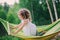 Happy child girl relaxing in hammock on summer camp in forest. Outdoor seasonal activities