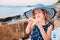 Happy child girl in stripe hat playing on the beach and listen to sea shell.