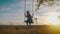 Happy child girl on swing at golden summer sunset. Silhouette of a young teenager girl swinging on the lone tree at