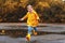 Happy child girl with an umbrella and rubber boots in puddle o