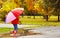 happy child girl with umbrella walking through puddles after autumn rain