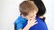 Happy child hugging his mom, touching his neck, sitting on a white sofa