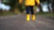 Happy child legs in yellow rubber boots walking down the road in autumn