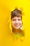 Happy child looks into the camera lens on a yellow background