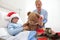 Happy child lying in bed in hospital room with Santa Claus hat and nurse dressing a teddy bear during Christmas holiday